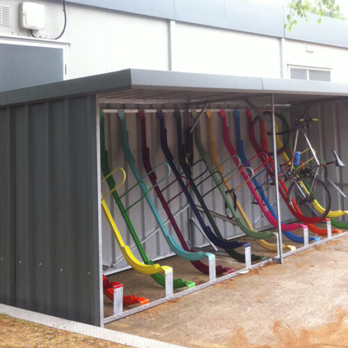 A metal bike storage shelter with multi coloured vertical bike storage racks inside.
