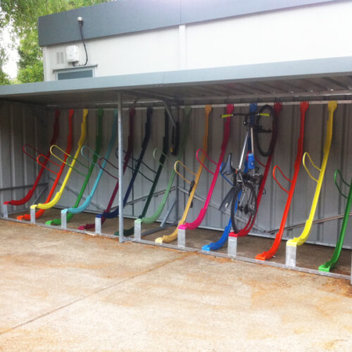 Rows of vertical metal bike storage racks in different primary colours under a metal shelter.