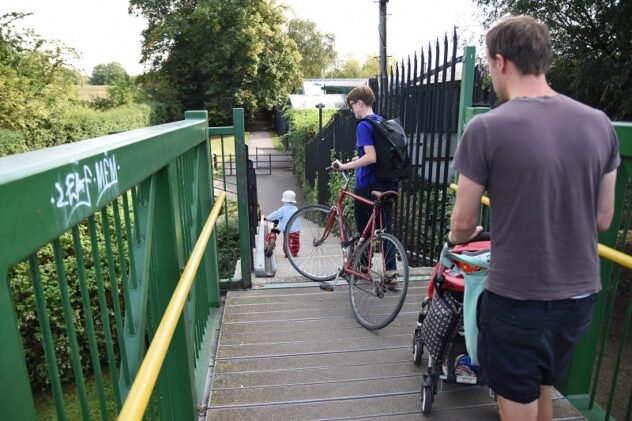 Three people walk down an outdoor staircase, two wheeling bikes and one with a pram.