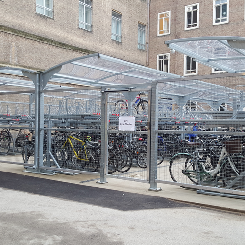 Rows of many bikes parked in a gated, undercover cycle shelter at Cambridge..