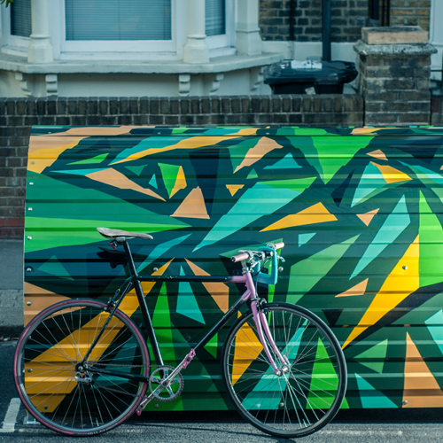 A bike leaning against a dome-roofed Bikehangar bike storage container painted in a funky green and gold geometric design.