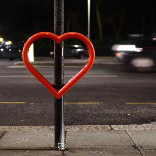 A red heart-shaped Lovehoop cycle stand, affixed to a street post.