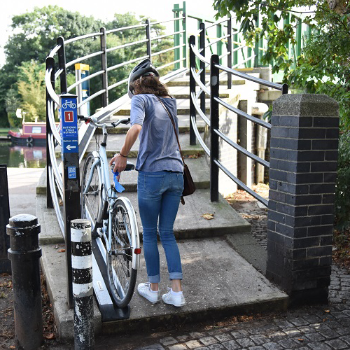 A woman wheels her bike up a ramp that adjoins a public outdoor staircase.