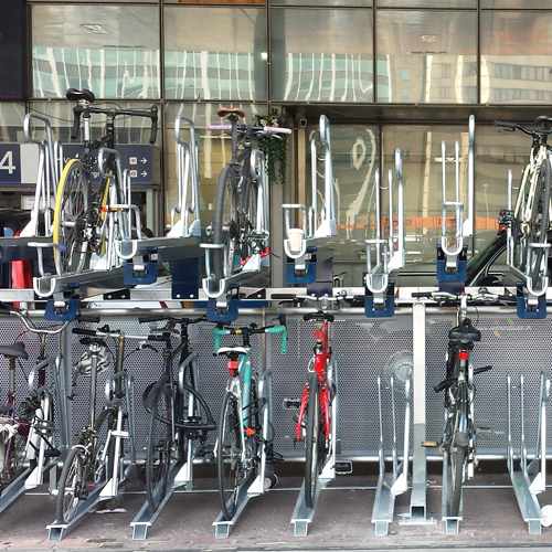 Bicycles stored on a two-layer bike storage rack outside a glass-walled building.