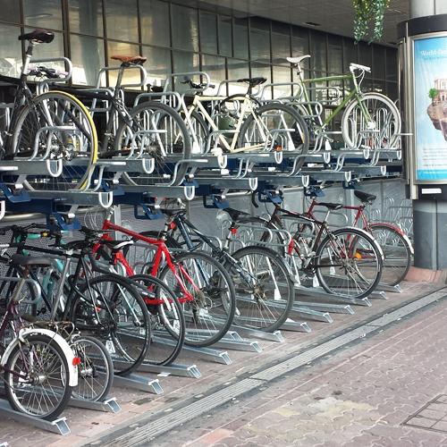 A two-tier bike storage rack on the side of a footpath, full of bikes.