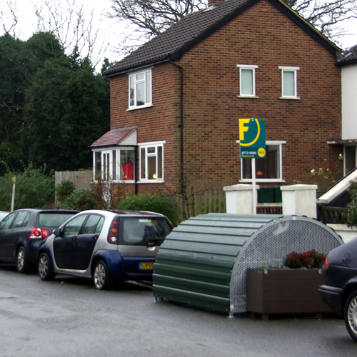 A dome-roofed Bikehangar bike storage container with cars parked either side on a residential street.