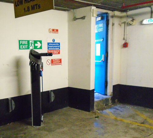 A tall, cylindrical public bike repair station next to an emergency exit.