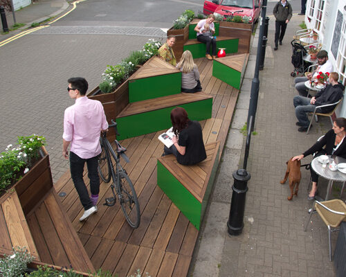 People sit outside a cafe on chairs and on benches in a street car park that has been converted into a green space.