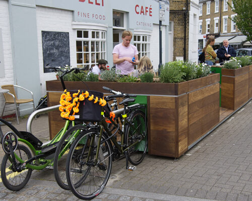 Bikes parked against metal racks of a Cyclehoop Parklet attached to the wooden planters of a Cyclehoop Parklet in Hammersmith and Fulham, London.