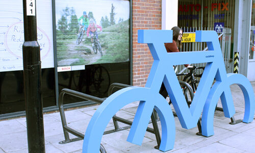 A blue Bike Port bike storage rack bolted to the pavement, in the shape of a bicycle.