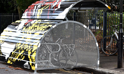 A Bikehangar bike storage container with perforated metal sides and a funky graffiti design on its domed roof.