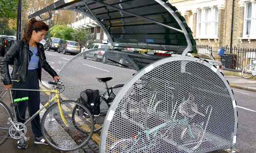A woman parks her bike inside a dome-roofed Bikehangar bike storage container on a residential street.