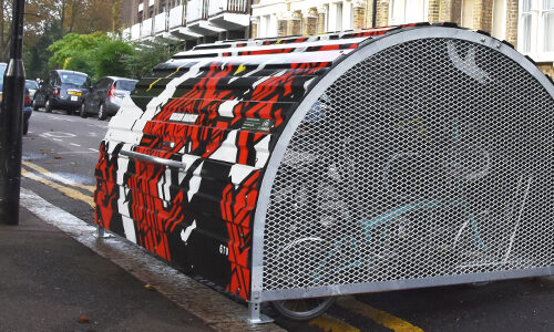 A Bikehangar bike storage container with perforated metal edges and a funky black, white and red geometric pattern painted onto its domed roof.