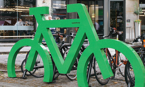 A green Bike Port bike storage rack in the shape of a bicycle with bikes parked inside on an urban street.