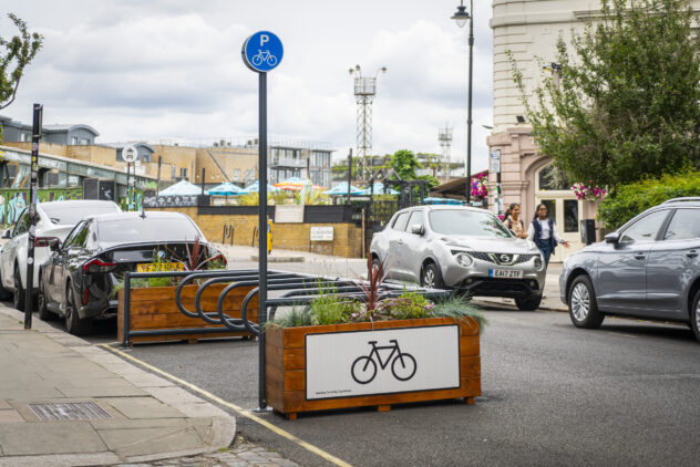 A row of metal bike racks between two wooden planters on the side of a road.