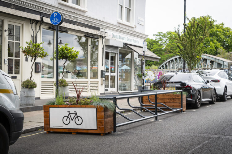 A metal bike rack flanked by wooden planter boxes in a car space on an urban street.