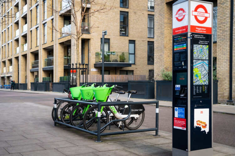 Three Lime bicycles parked in a bike park rack on an urban street, next to a sign that says Cycles.