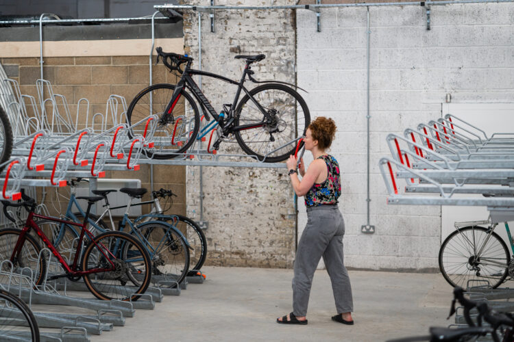 A woman pushes her bike into the second level of a two-layer bike storage rack.