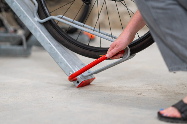 A person slots a bicycle wheel into a bike storage rack.