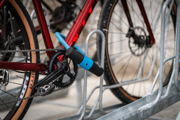 A red bicycle locked to a metal bike stand with a blue lock.