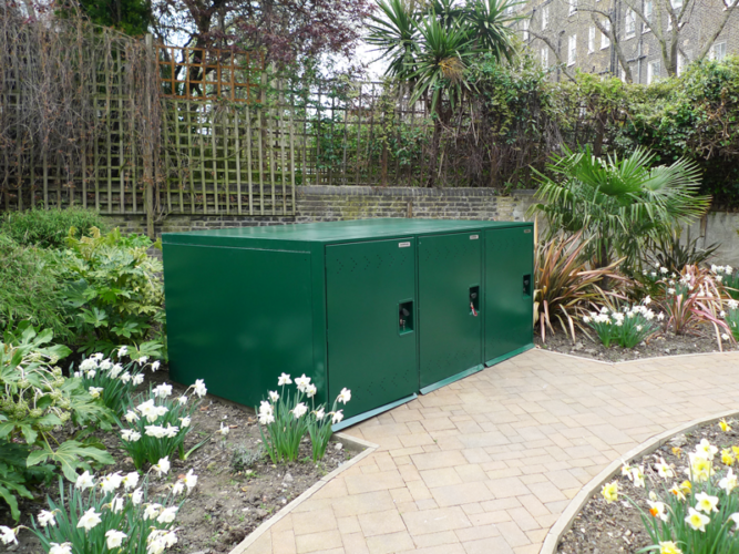 A rectangular green metal Bike Locker storage container in the middle of a garden.