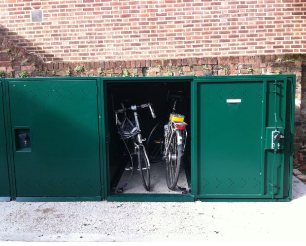 Two bikes inside a green metal Bike Locker rectangular storage container.