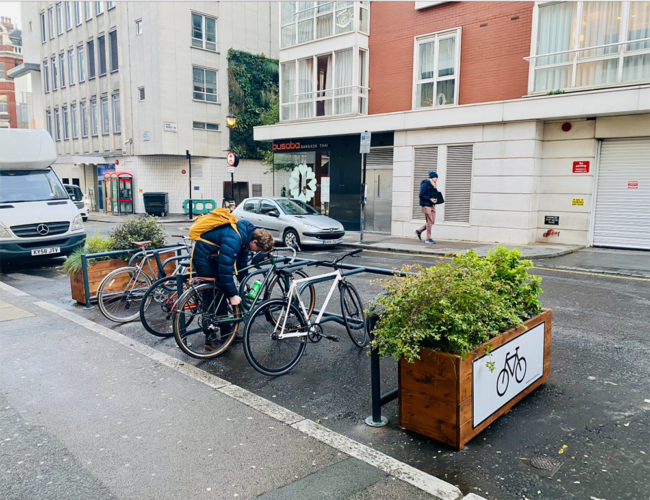 A person parks a bike against a metal rack between two wooden planters.