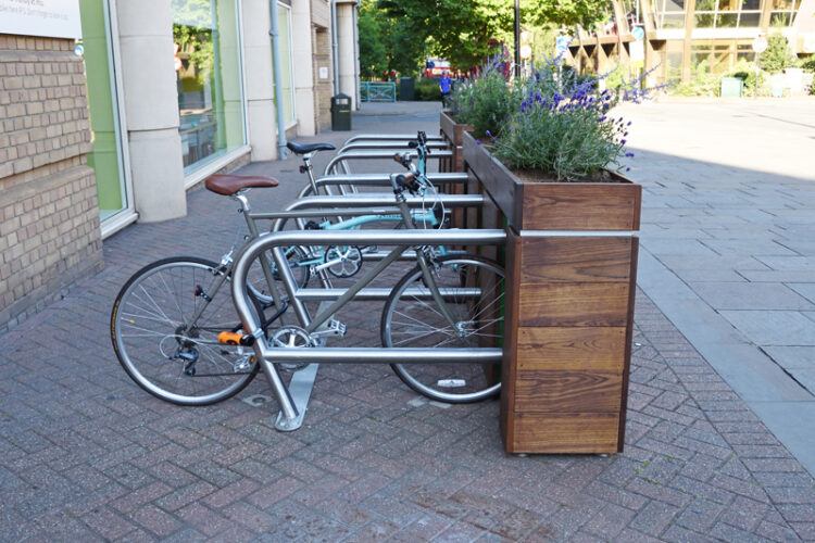 Bikes parked against metal racks attached to a wooden planter.