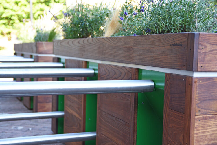 A close up of metal bike racks attached to a wooden planter.