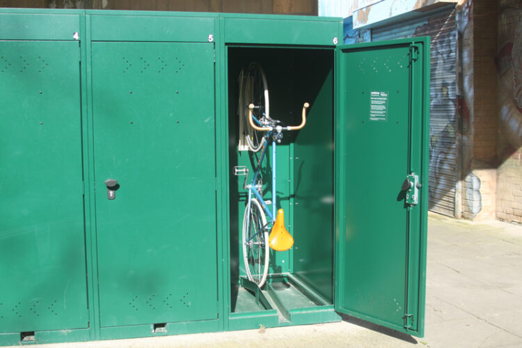 A bike stored vertically in a green metal bike locker.