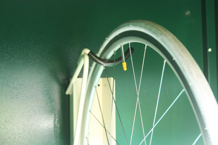 A bike wheel secured by a metal hook inside a vertical bike locker.