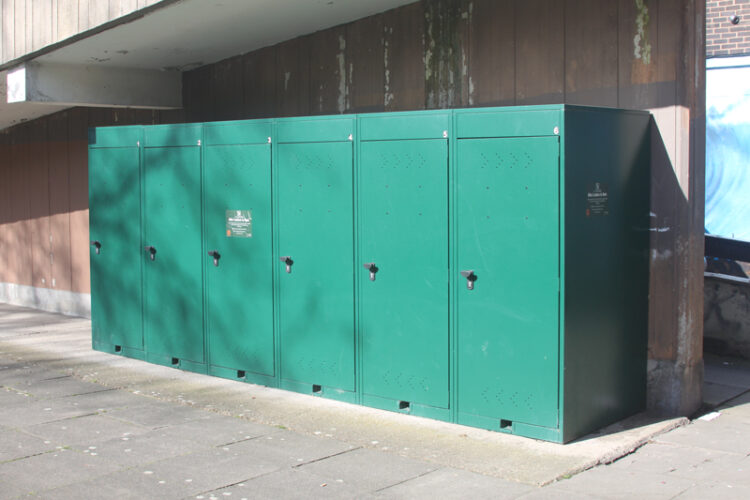 A green, rectangular, metal Vertical Bike Locker with six doors.
