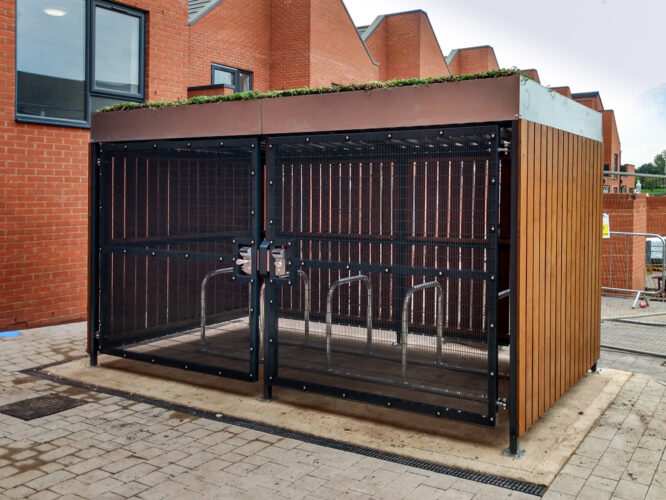 A rectangular Wood Bike Shelter with black metal grate doors, showing five metal bike stands inside.