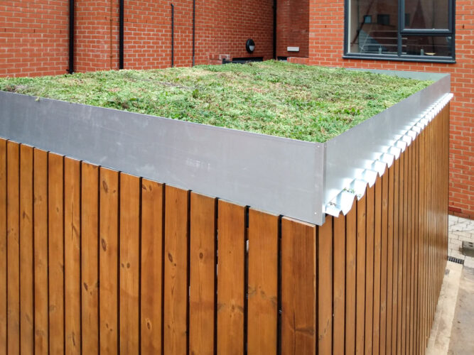 The green planted roof of a rectangular bike storage shed with wood panelled walls.