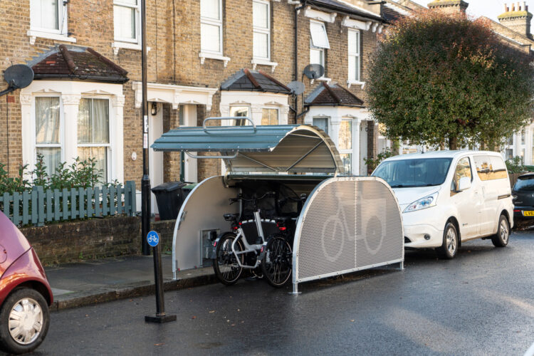A dome-roofed Bikehangar storage container on a residential street with the curved roof open to show bikes parked inside.