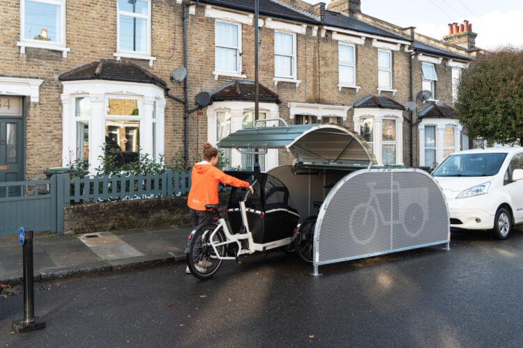 A person wheels their cargo bike into a dome-roofed Bikehangar storage container on a residential street.