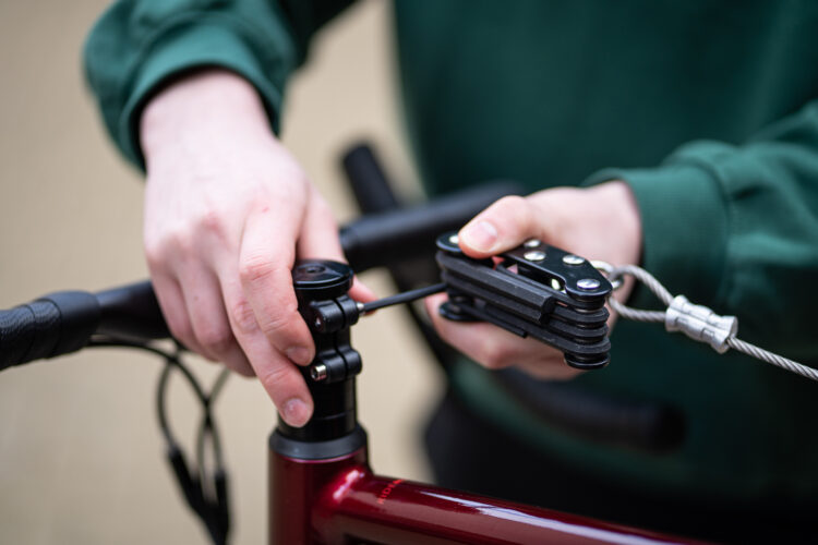 A close-up of a person's hands using a tool attached to a wire to adjust their handlebars.