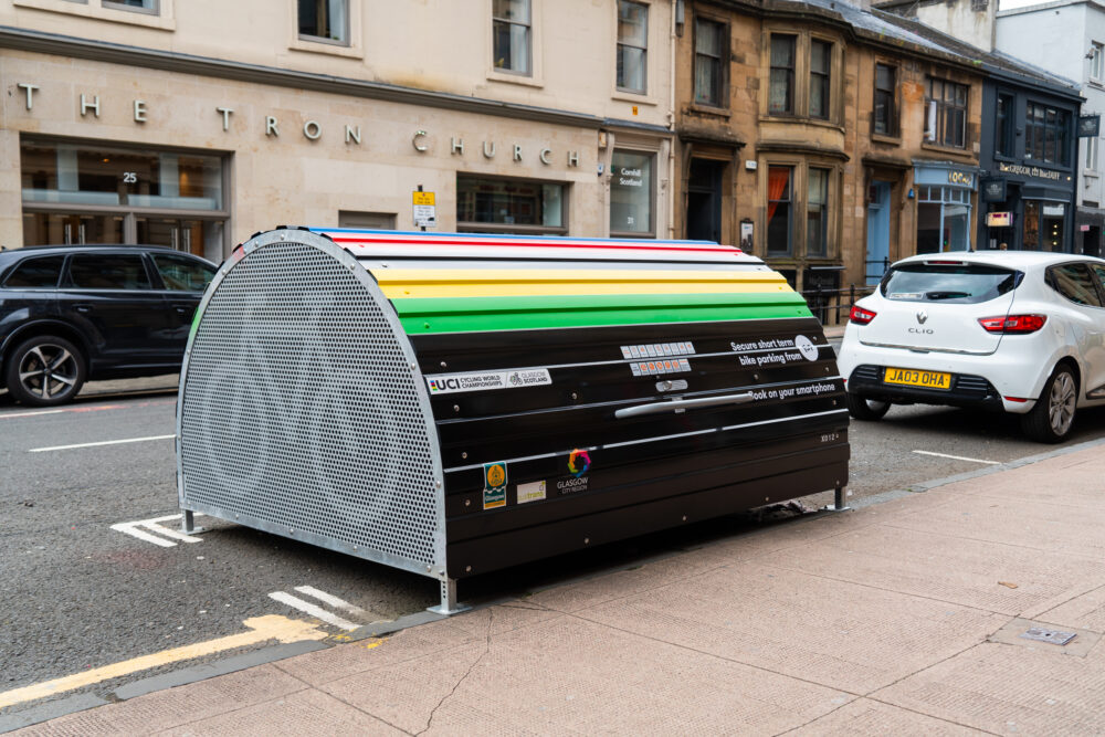 A dome-roofed Bikehangar bike storage container painted in multicoloured stripes.