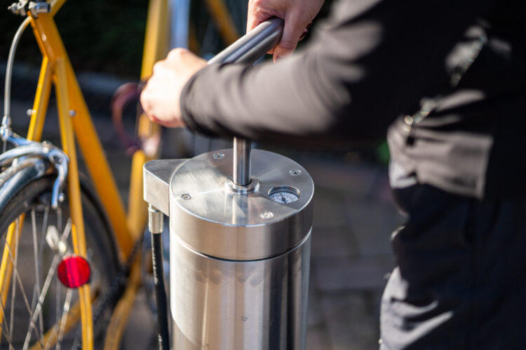 A person uses a metal bike tire pump with two hands.