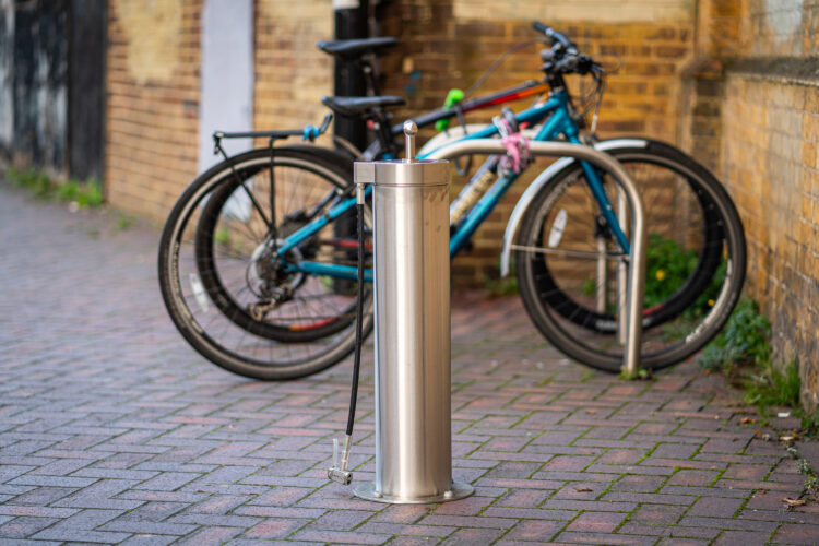 A tall cylindrical metal bike repair station with bikes parked in the background.