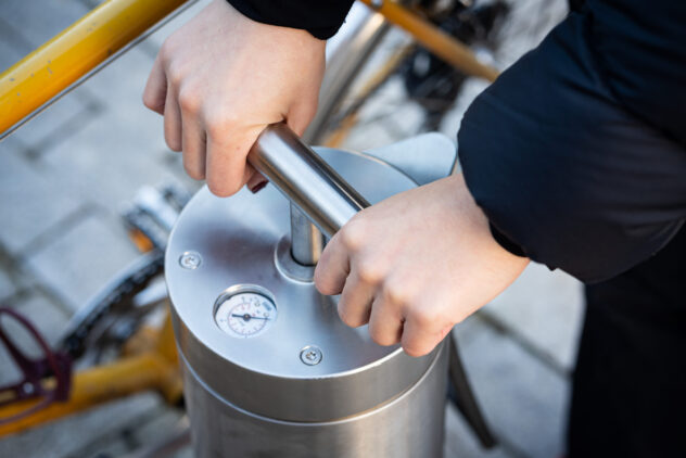 A person uses a metal bike pump with two hands.