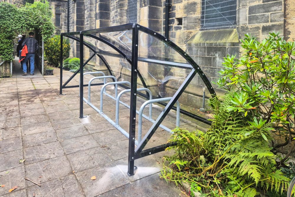 a clear bike shelter with bike racks by a school